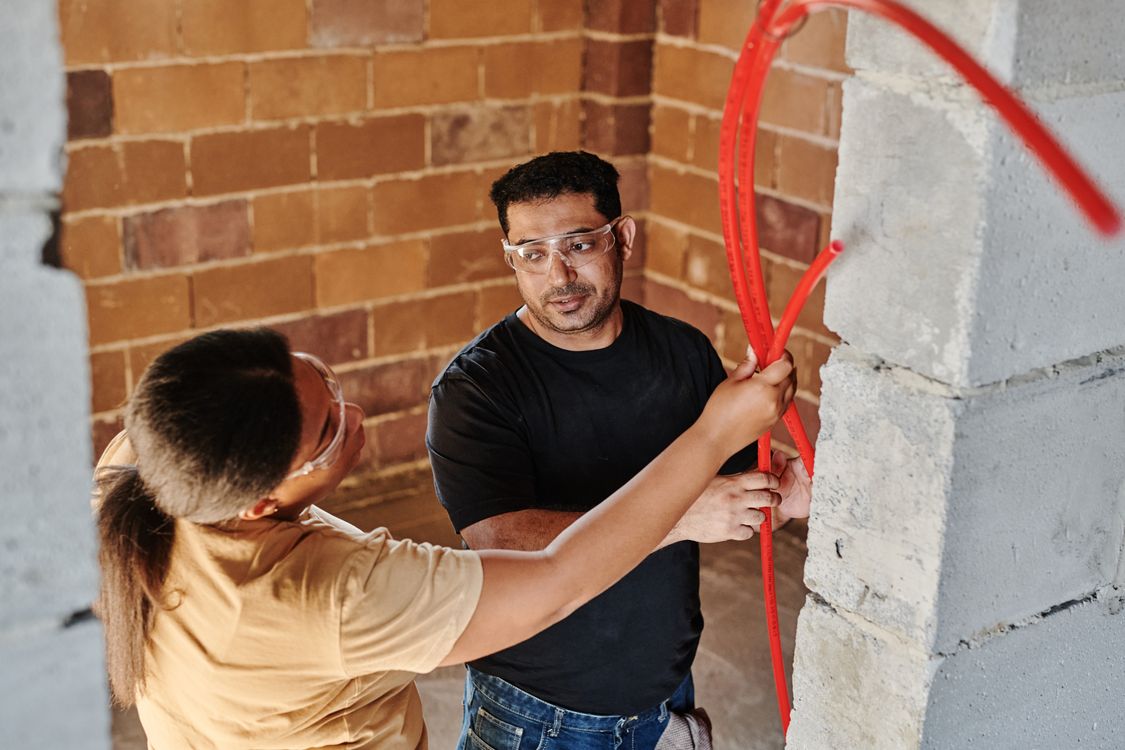 Two tradespeople working together to fit tubing at a renovation site.